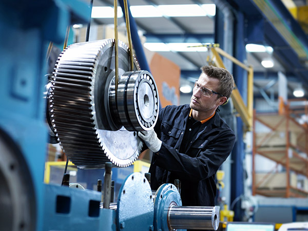 Man in protective gear inspects large industrial gear machinery in a factory setting